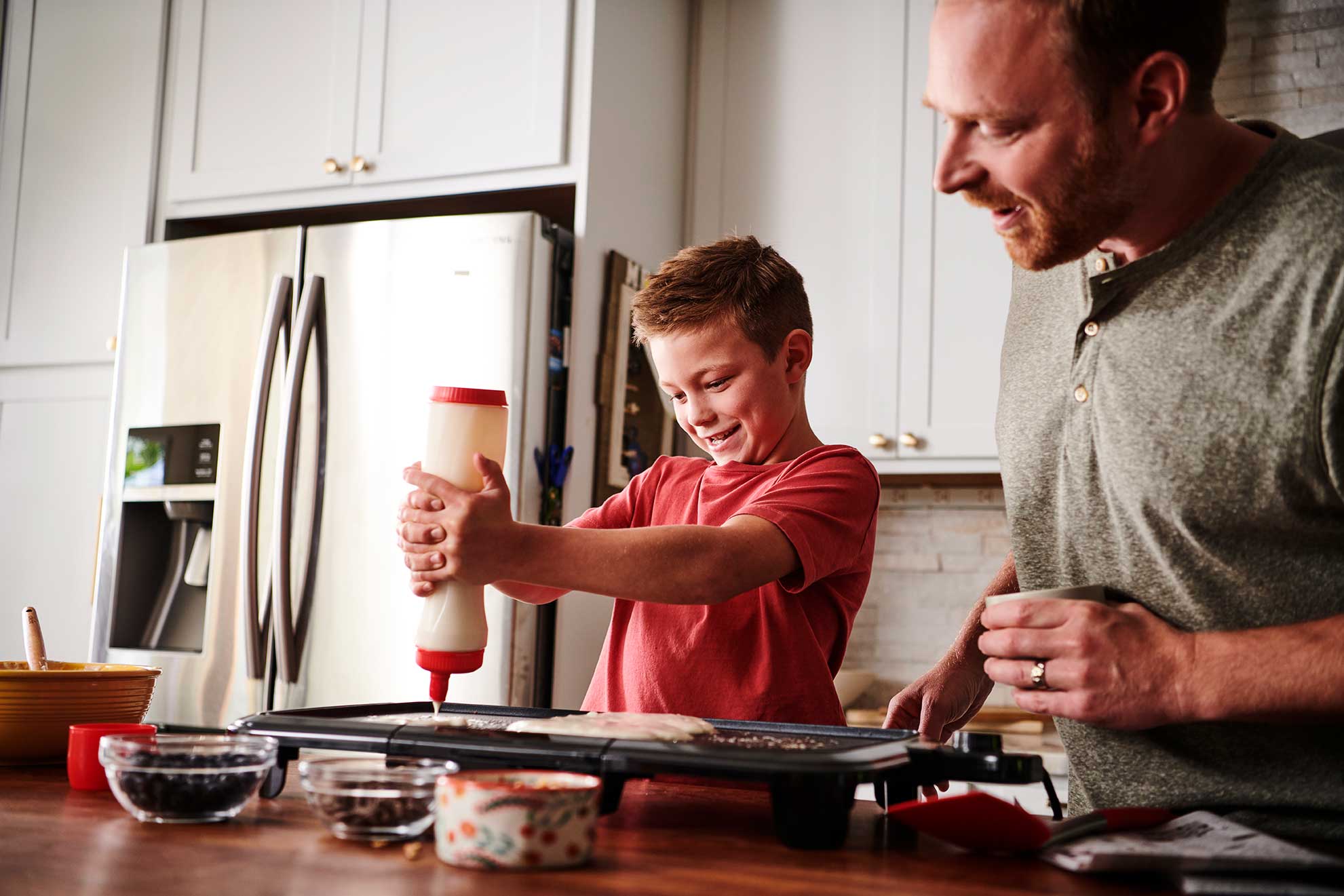 A happy kid squeezes buttermilk pancake batter onto a griddle.
