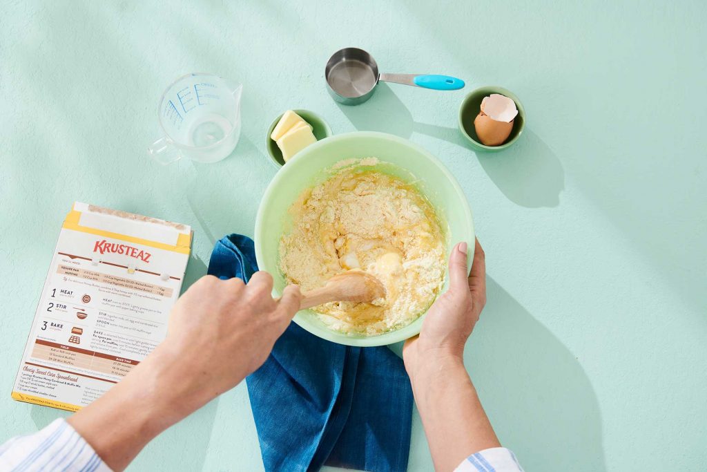 A person mixes Krusteaz cornbread mix in a green mixing bowl.